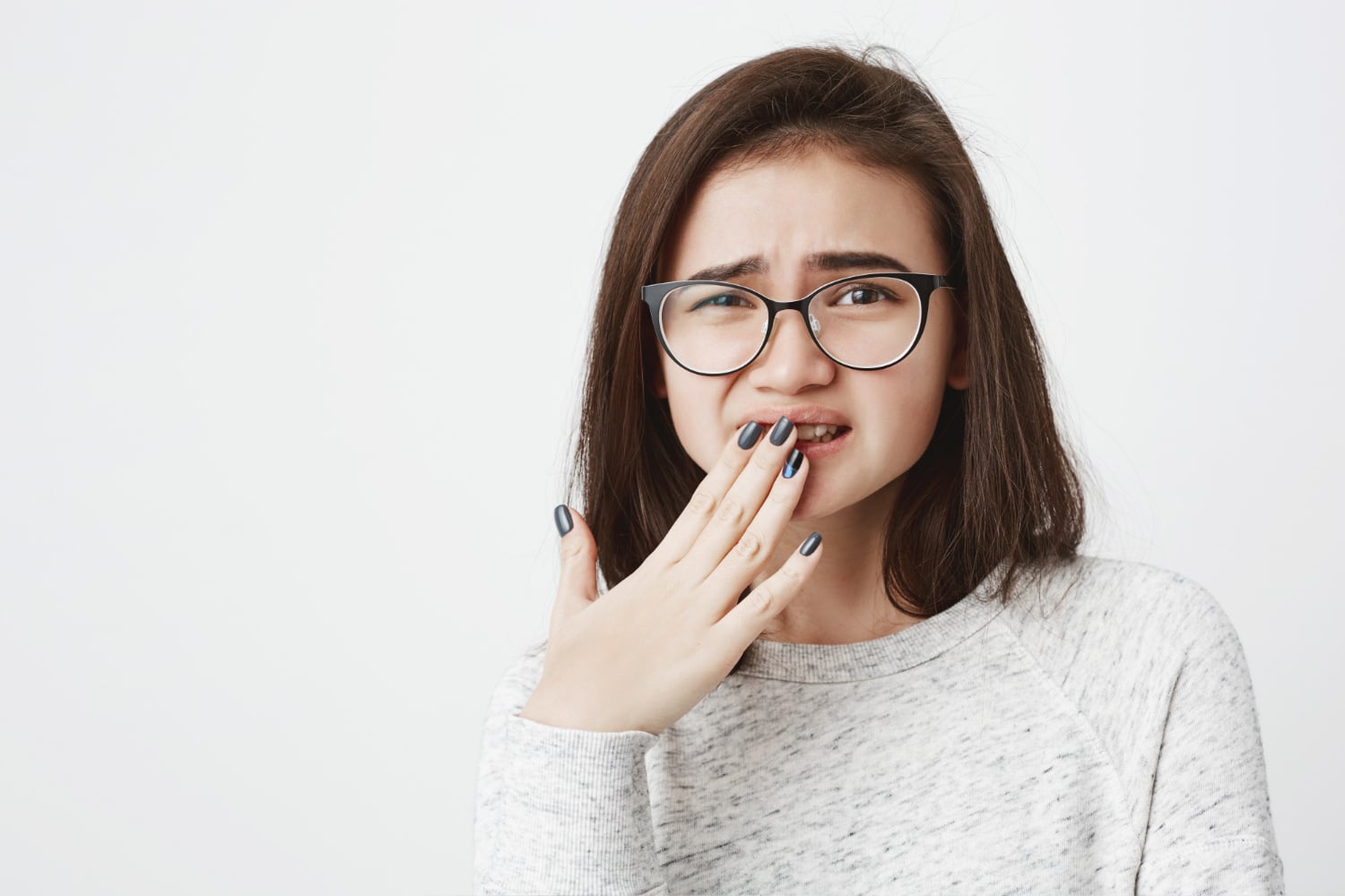 retrato-joven-linda-mujer-gafas-entrecerrando-ojos-cubriendo-su-boca-mano-sintiendo-dolor-o-pena Hiperdoncia: ¿Qué significa tener dientes de más y cómo se trata?